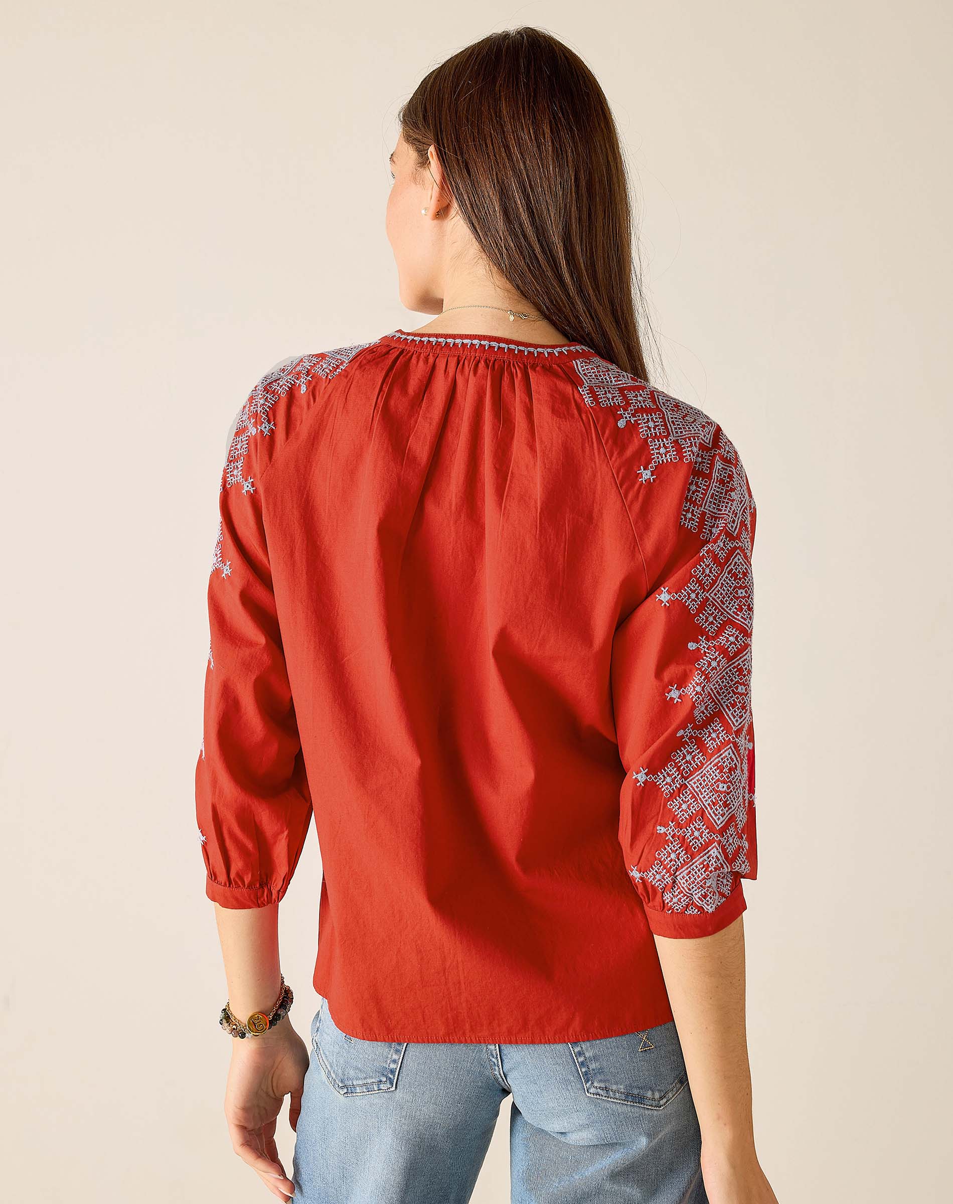 Red embroidered blouse worn by a person on a beige background