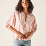 Woman wearing a pink blouse with lace details on a plain background
