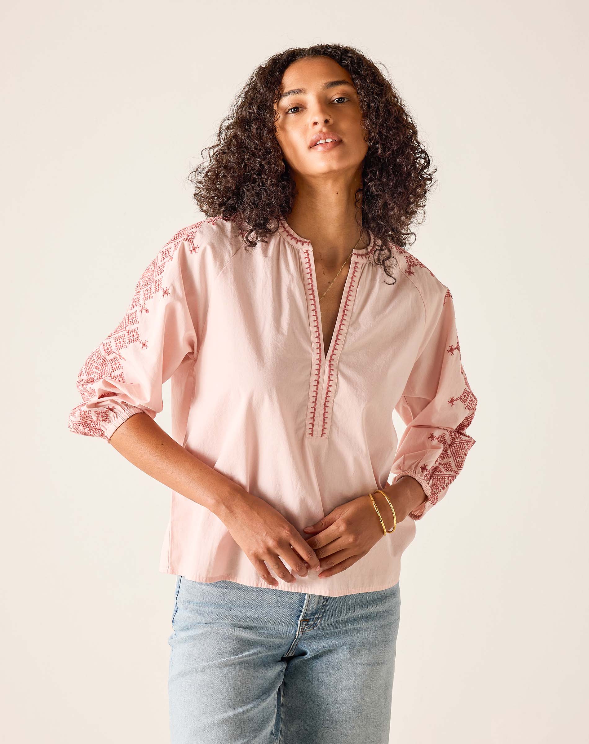 Woman wearing a pink blouse with lace details on a plain background
