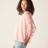 Woman wearing a light pink blouse with embroidery and light blue jeans against a beige background