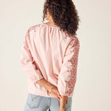 Person wearing a pink blouse with lace details on a plain background
