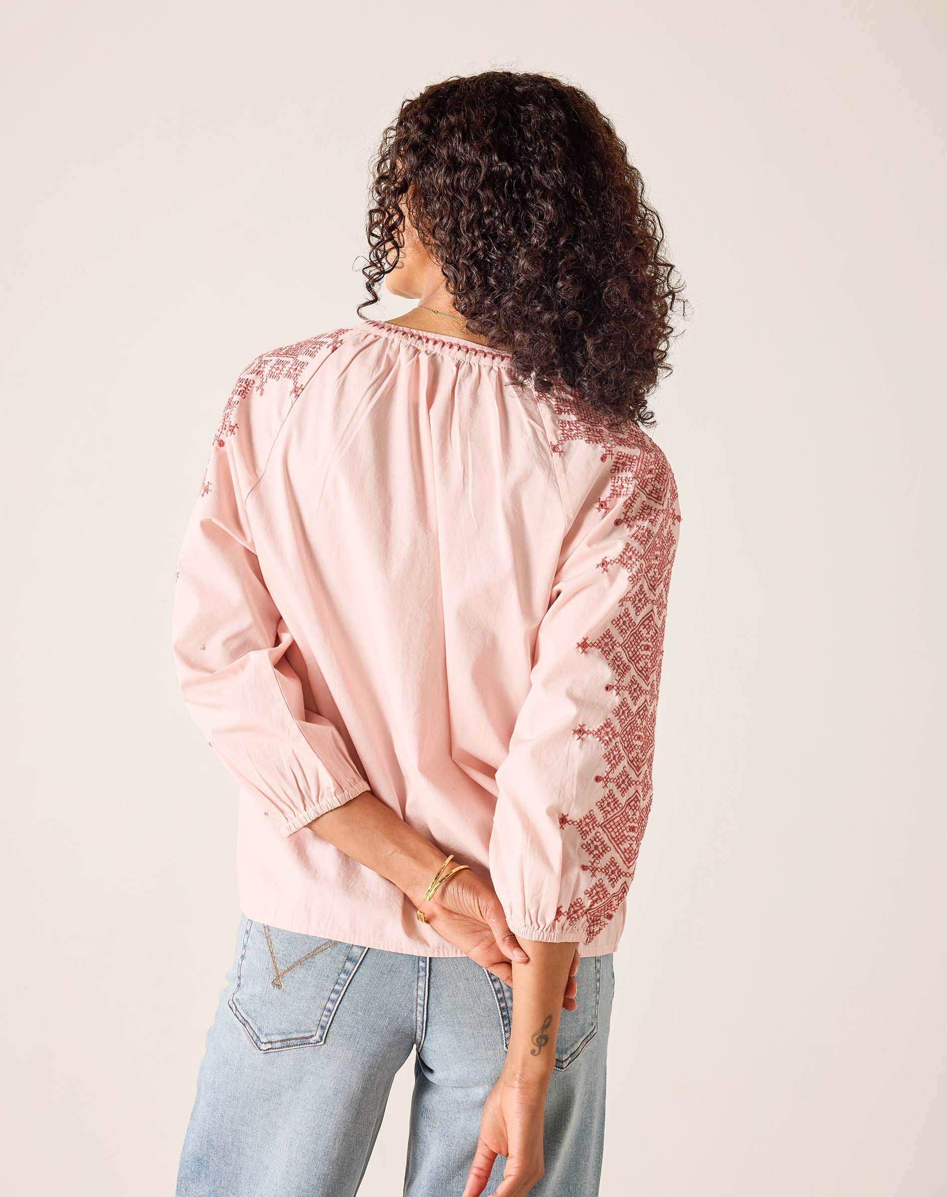 Person wearing a pink blouse with lace details on a plain background
