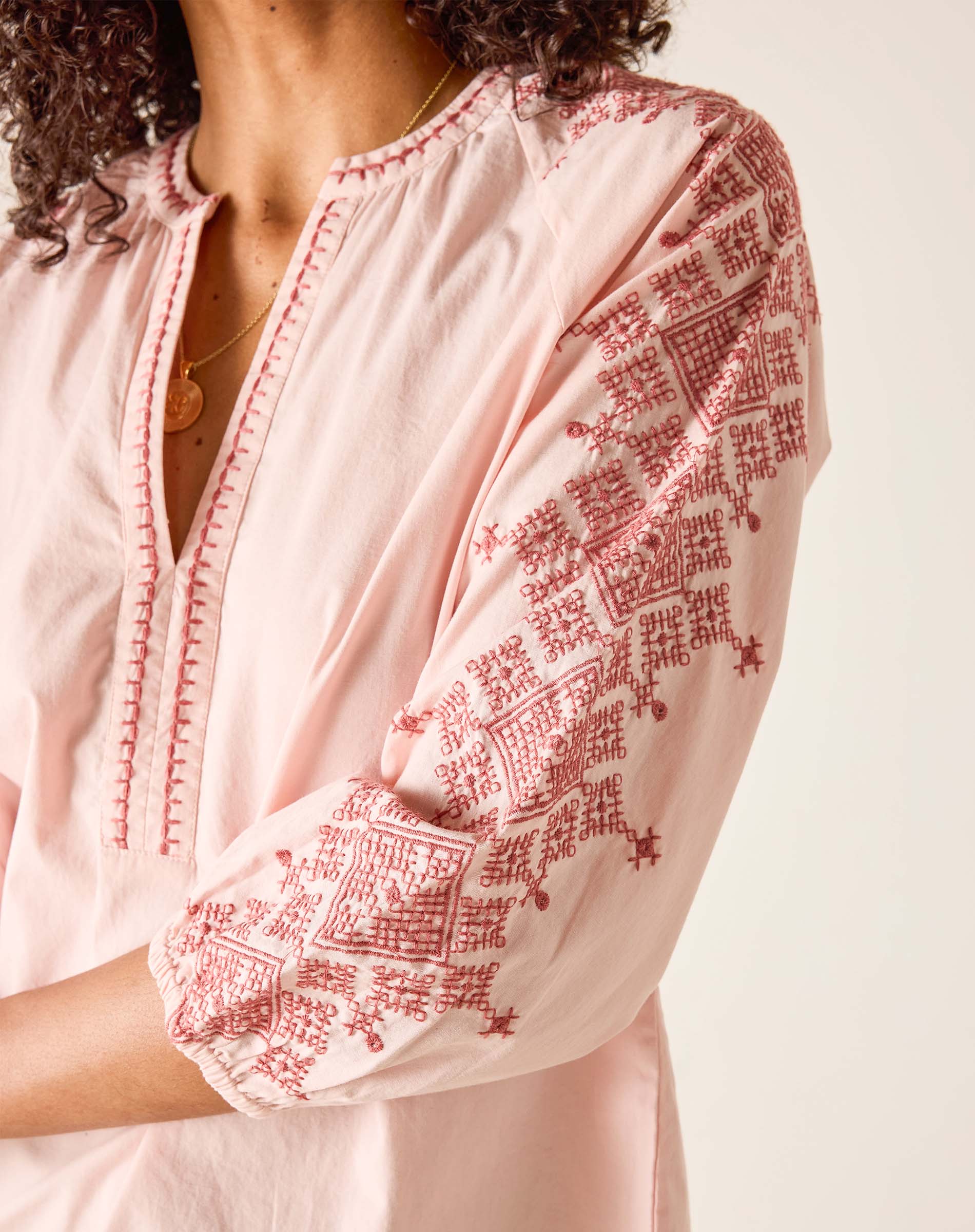Light pink blouse with red embroidery on a plain background