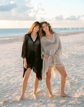 two females standing on the beach wearing white and black poncho cover up with front pockets
