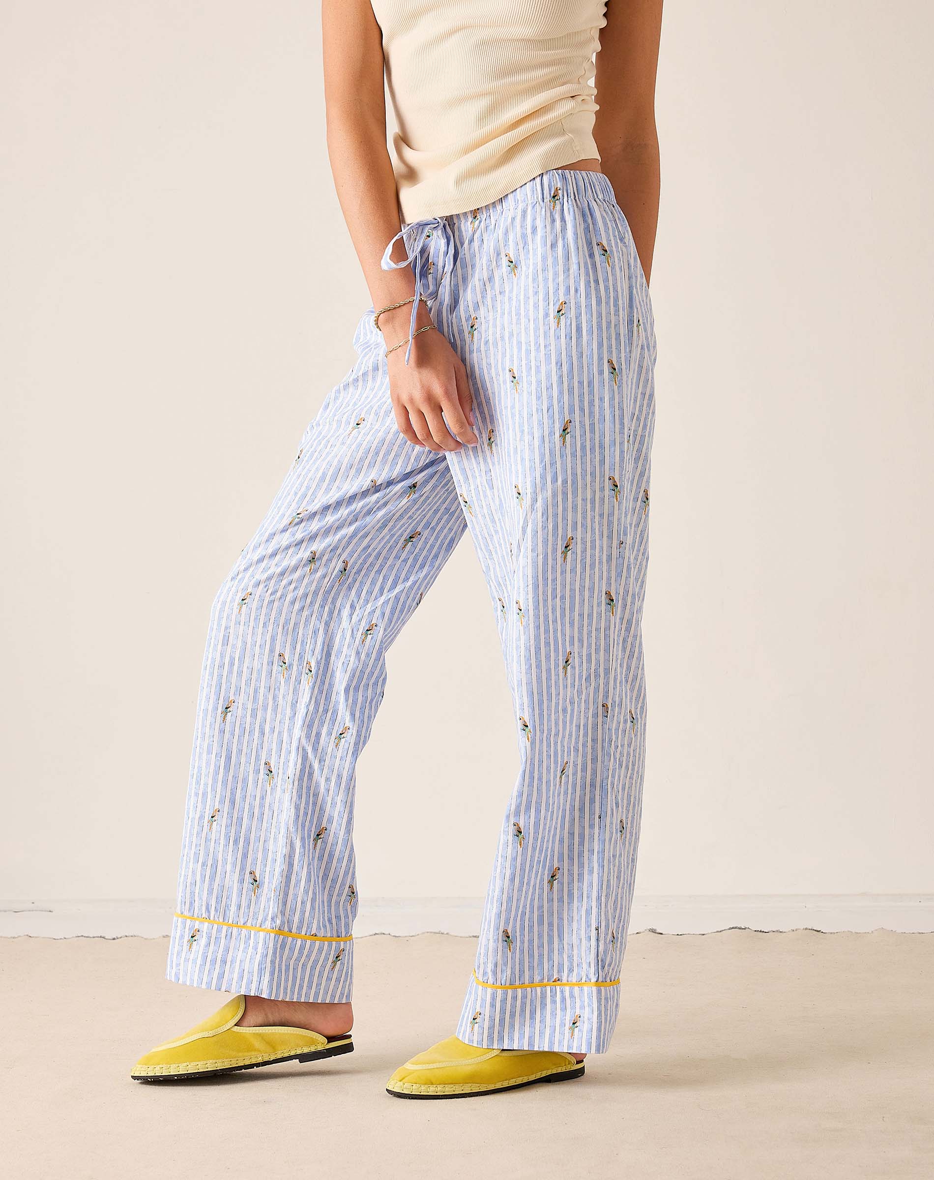 Person wearing blue striped pajama pants with yellow trim on a beige background