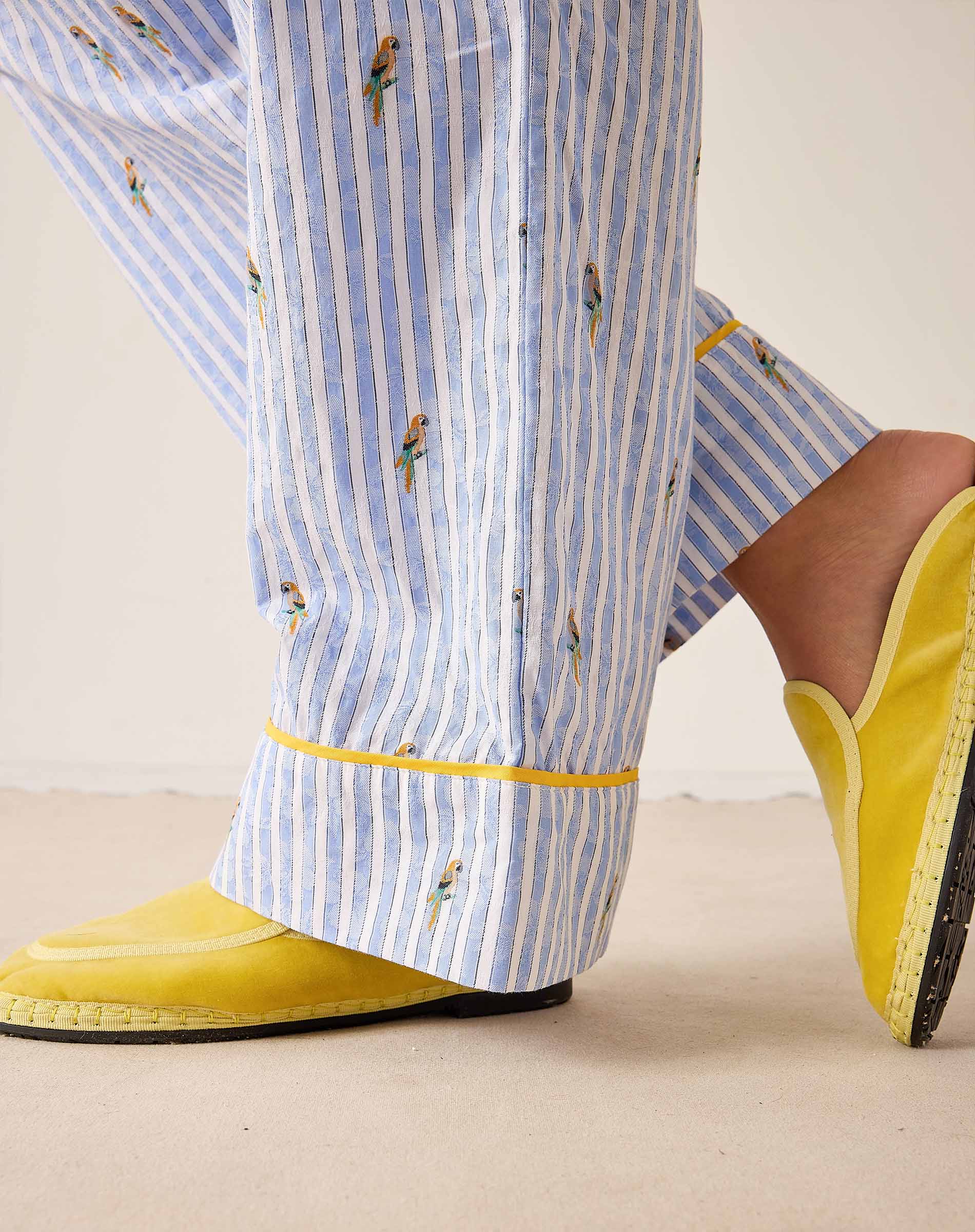 Person wearing blue and white striped pants with yellow trim and yellow shoes on a beige background