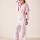 Woman wearing a pink and white patterned pajama set with a matching cardigan on a beige background