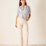 Woman wearing a striped shirt and beige pants against a plain background