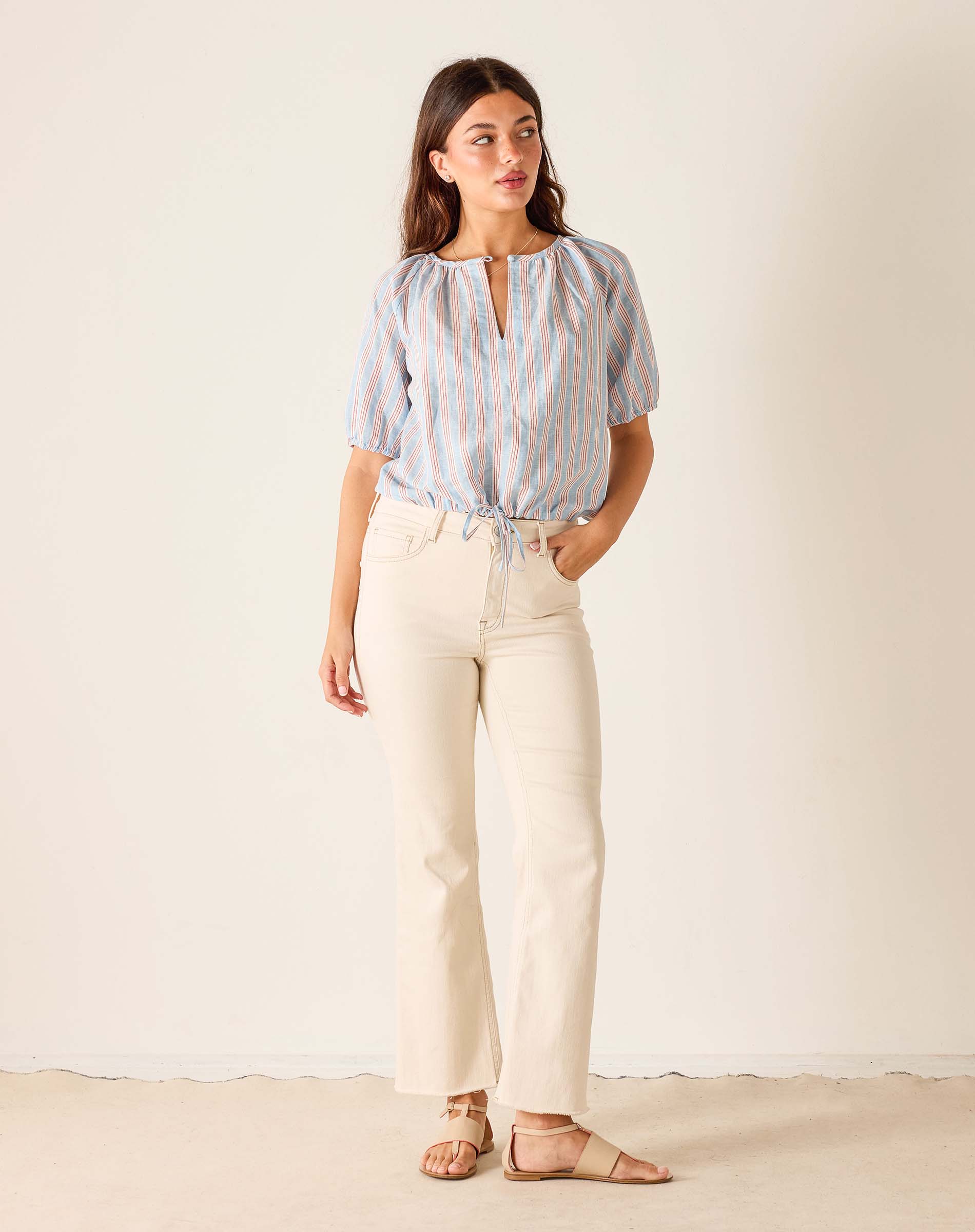 Woman wearing a striped shirt and beige pants against a plain background