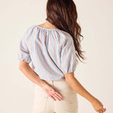 Woman wearing a striped blouse and beige pants against a plain background