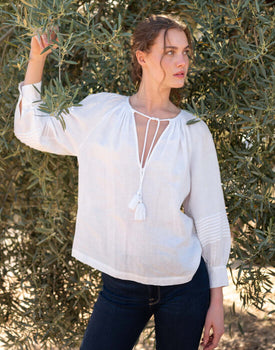 female wearing white linen blouse with dark jeans standing under an olive tree in spain