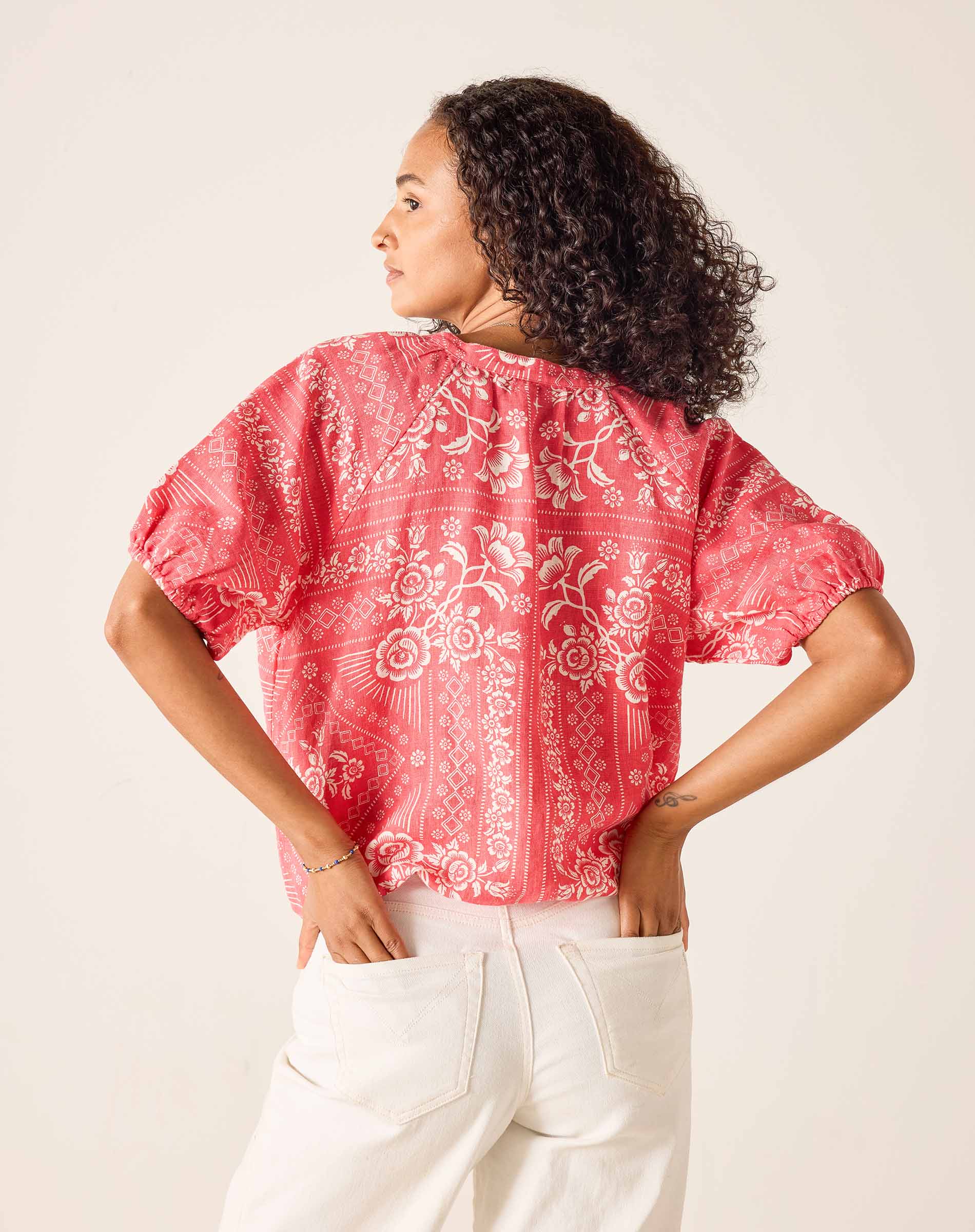 Woman wearing a red patterned blouse with white pants on a plain background