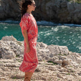 Woman in a red dress standing on rocky cliffs overlooking the ocean.