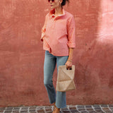 Woman in a pink checkered shirt and blue jeans standing against a textured red wall.