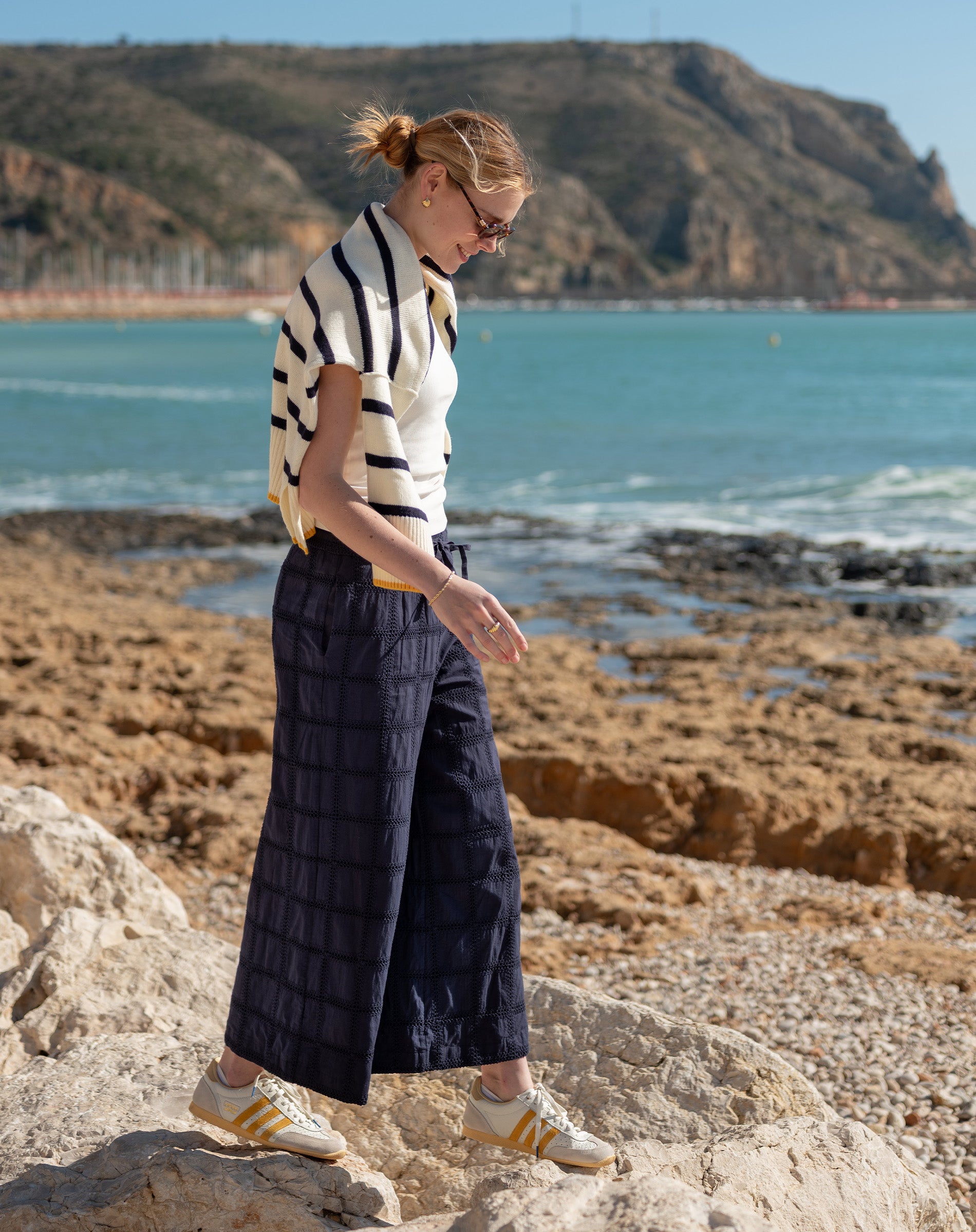 Woman standing on a rocky beach with ocean and cliffs in the background