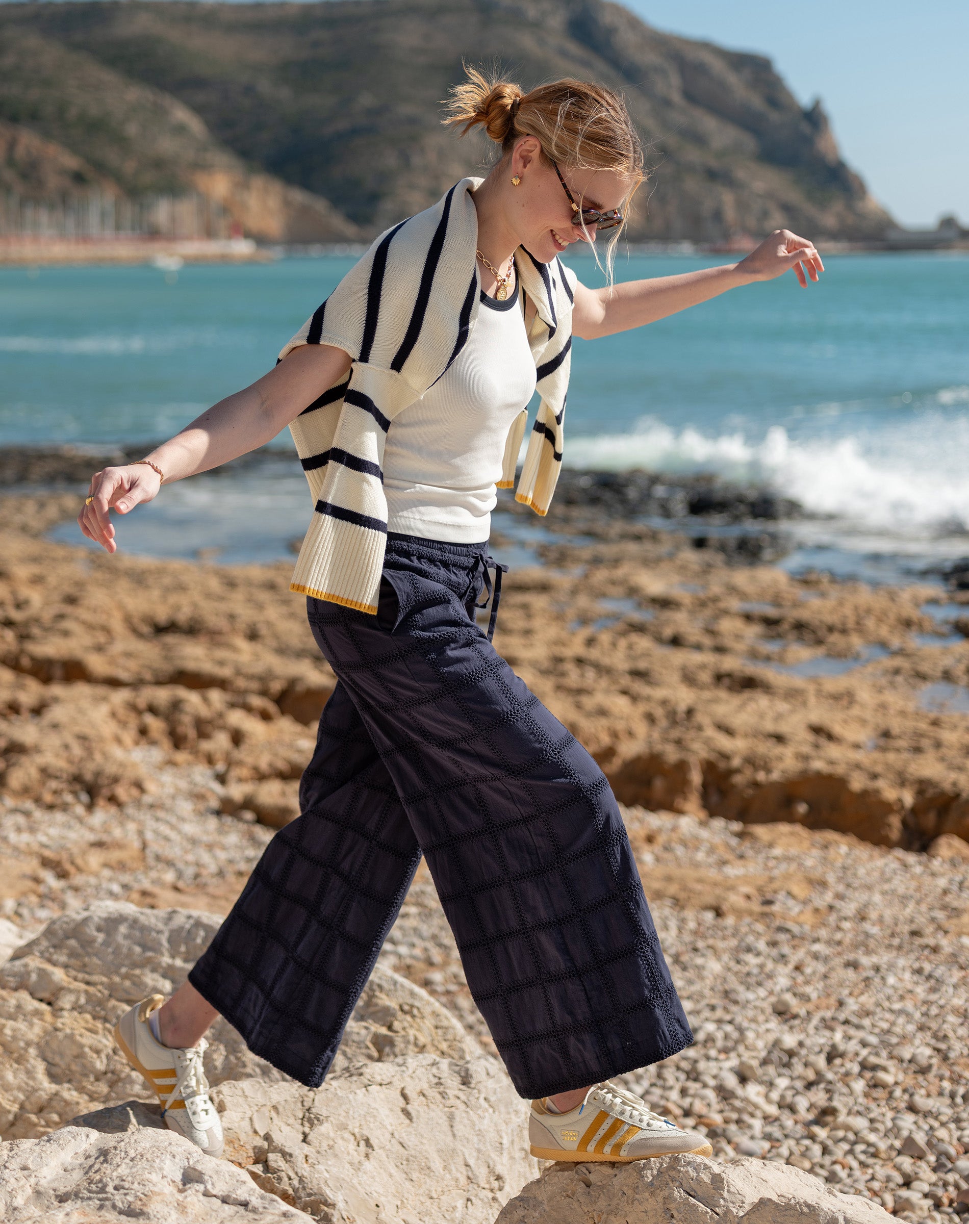 Woman walking on rocks by the ocean with mountains in the background