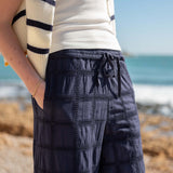 Person wearing navy checkered pants with a blurred beach background