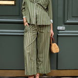 Person wearing a green and white striped outfit with wide-leg pants, standing against a dark green door.