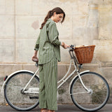 Woman in a green striped outfit standing next to a bicycle with a basket against a stone wall.