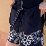 Navy blue shorts with white floral embroidery on a beige background