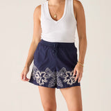 Woman wearing a white tank top and navy skirt with white patterns on a plain background