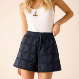 Person wearing navy checkered shorts and a white top on a beige background