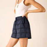 Woman wearing a white tank top and navy checkered skirt on a beige background