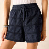 Navy blue shorts with eyelet details worn by a person on a beige background