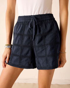 Navy blue shorts with eyelet details worn by a person on a beige background