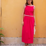 Woman wearing a red dress with white trim against a yellow wall.