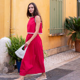 Woman in a red dress standing on a street with a yellow wall and plants in the background