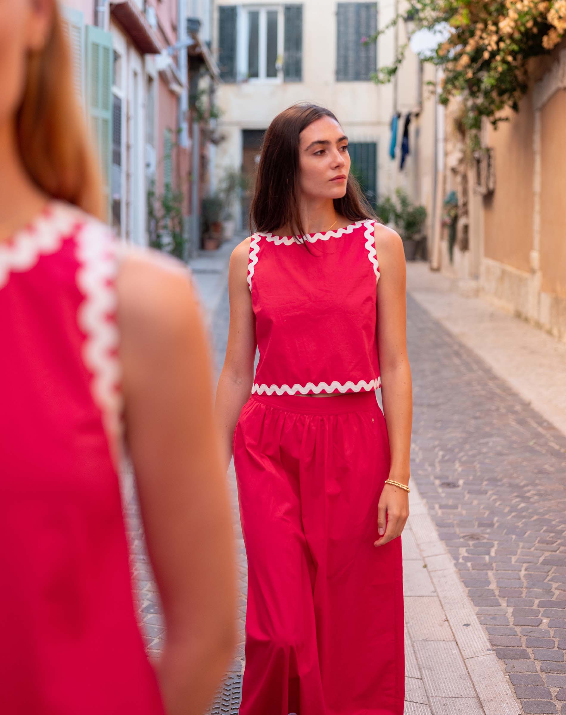 Woman in a red outfit standing on a narrow street with buildings on either side.