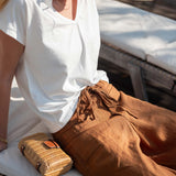 Woman sitting on a boat wearing a white shirt and brown pants, with a woven bag beside her.