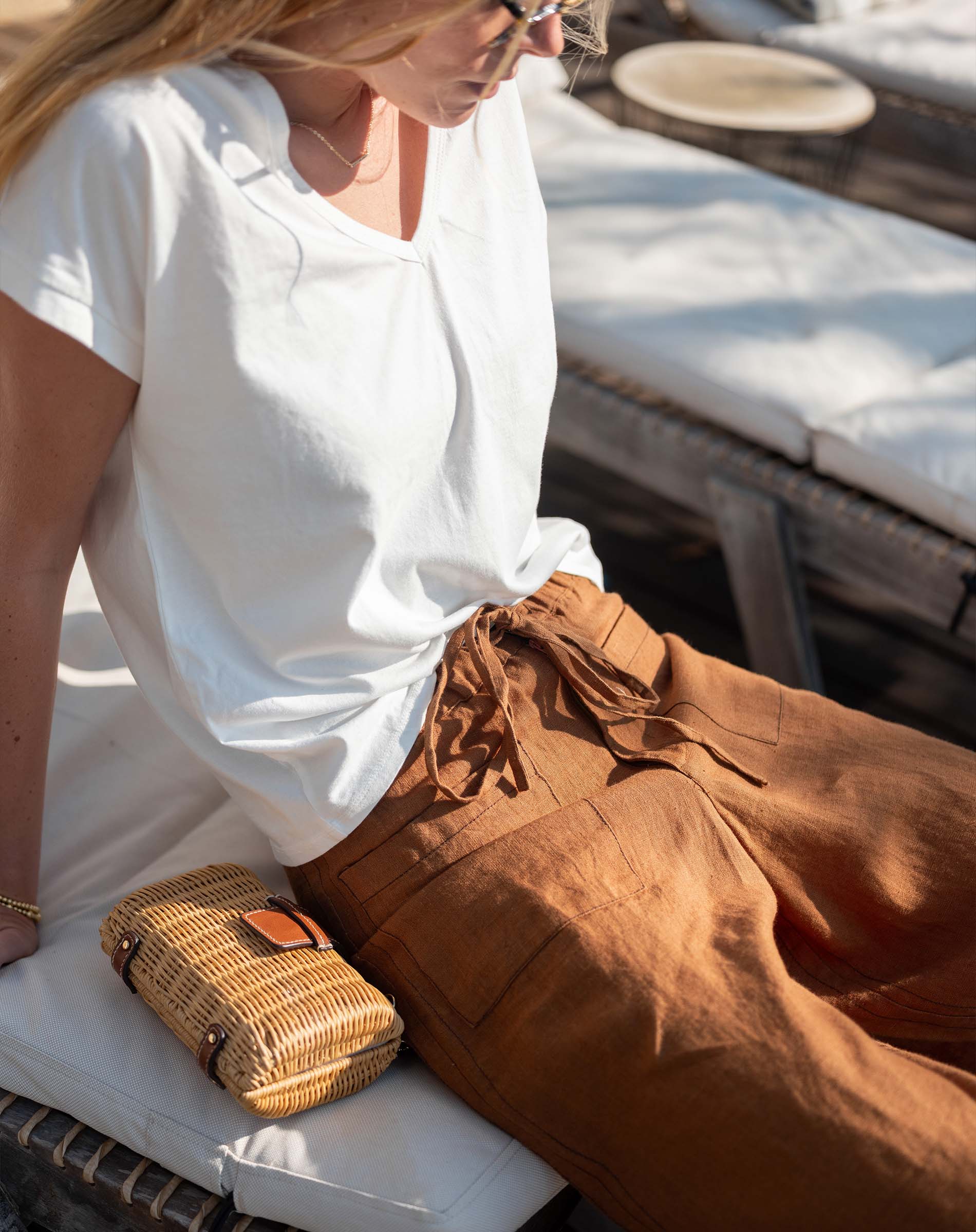 Woman sitting on a boat wearing a white shirt and brown pants, with a woven bag beside her.