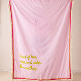 Pink textured blanket with yellow text and red trim on a light background