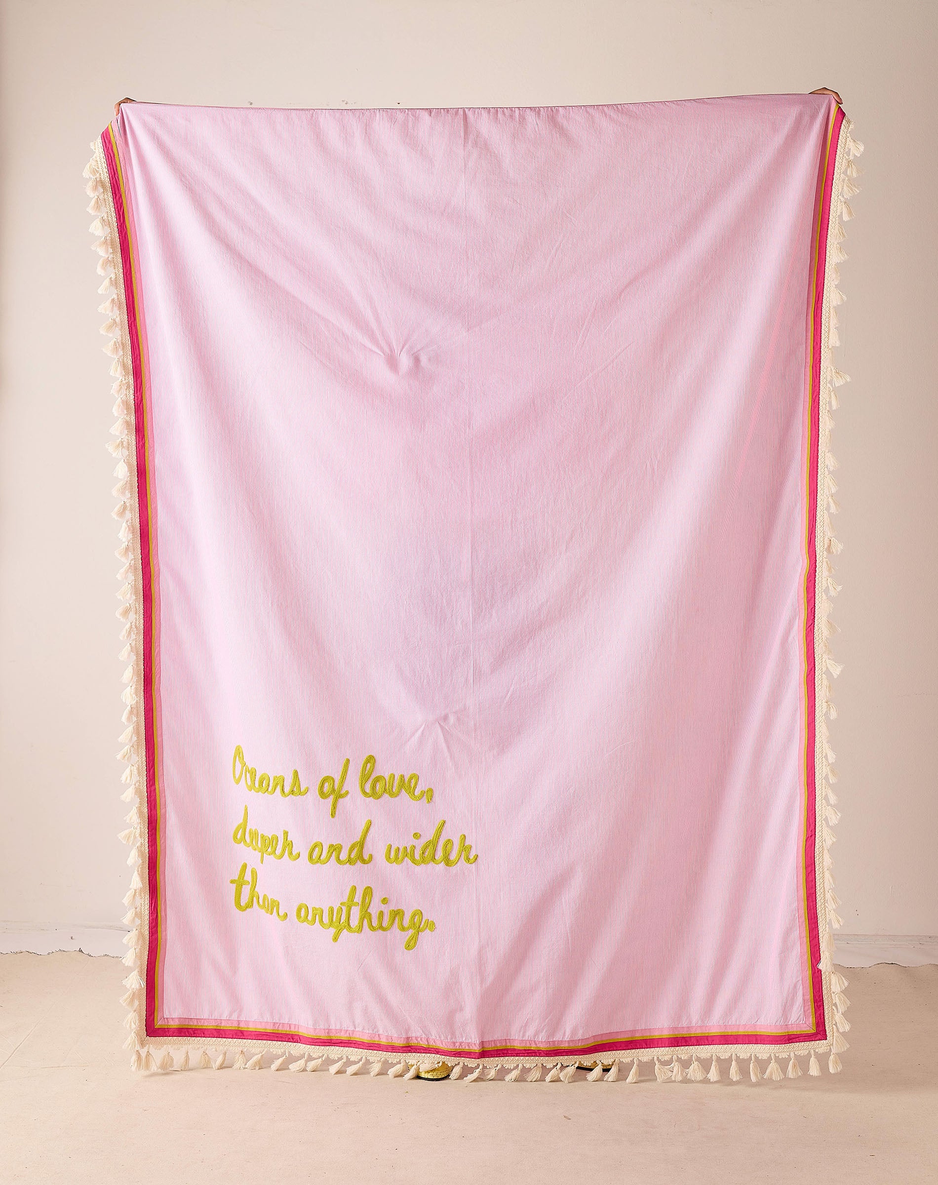 Pink textured blanket with yellow text and red trim on a light background