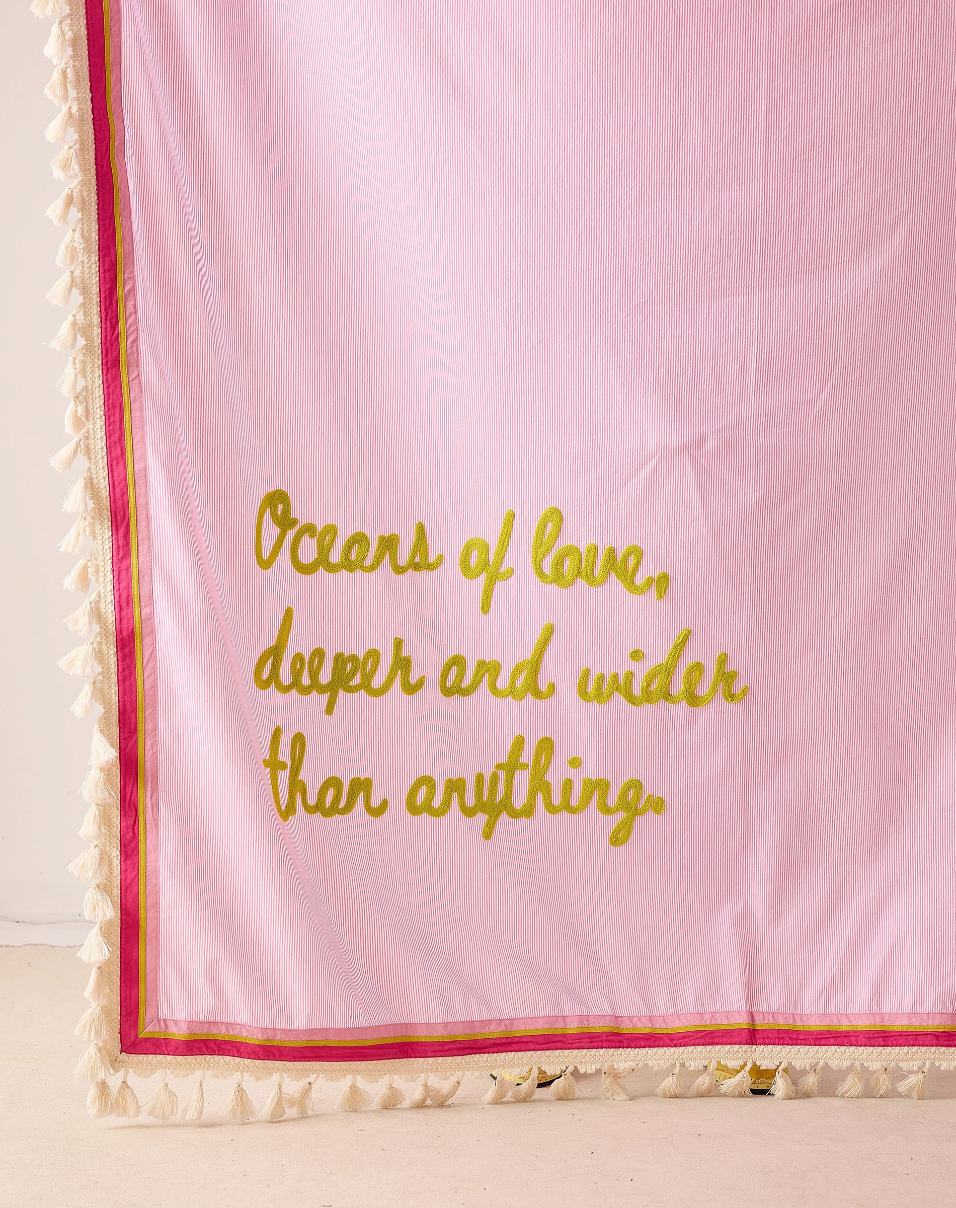 Pink blanket with chartreuse text  that says "oceans of love, deeper and wider than anything" with a natural tassel trim 