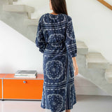 Woman wearing a blue patterned dress standing in a modern interior setting with an orange cabinet.
