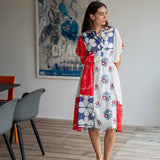 Woman wearing a colorful dress with floral patterns in a room with chairs and a painting on the wall.
