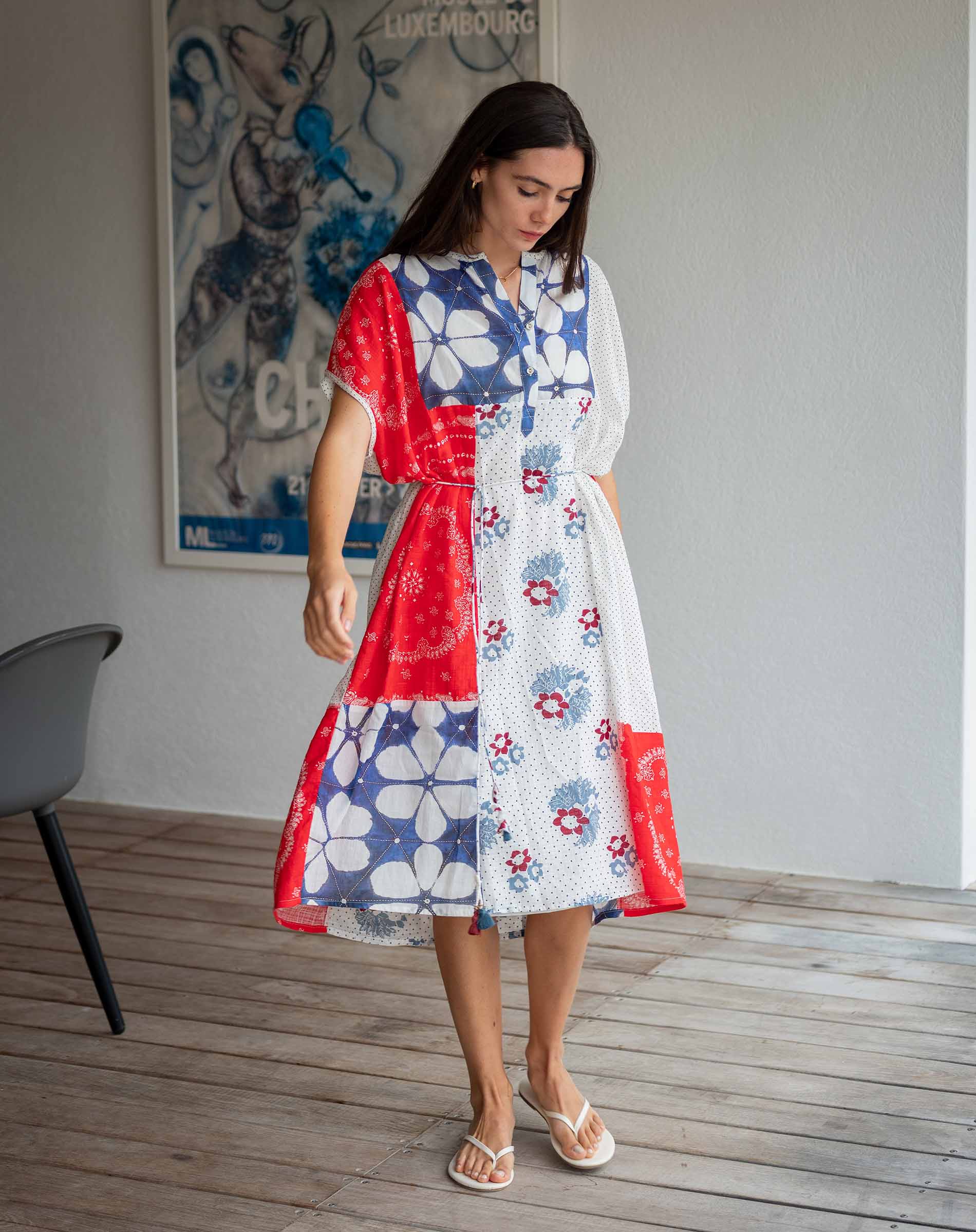 Woman wearing a colorful dress with abstract patterns in a room with a poster on the wall.