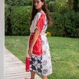Woman wearing a red, white, and blue floral dress standing on a wooden path with greenery in the background