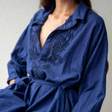 Woman wearing a blue dress with intricate detailing on a plain background