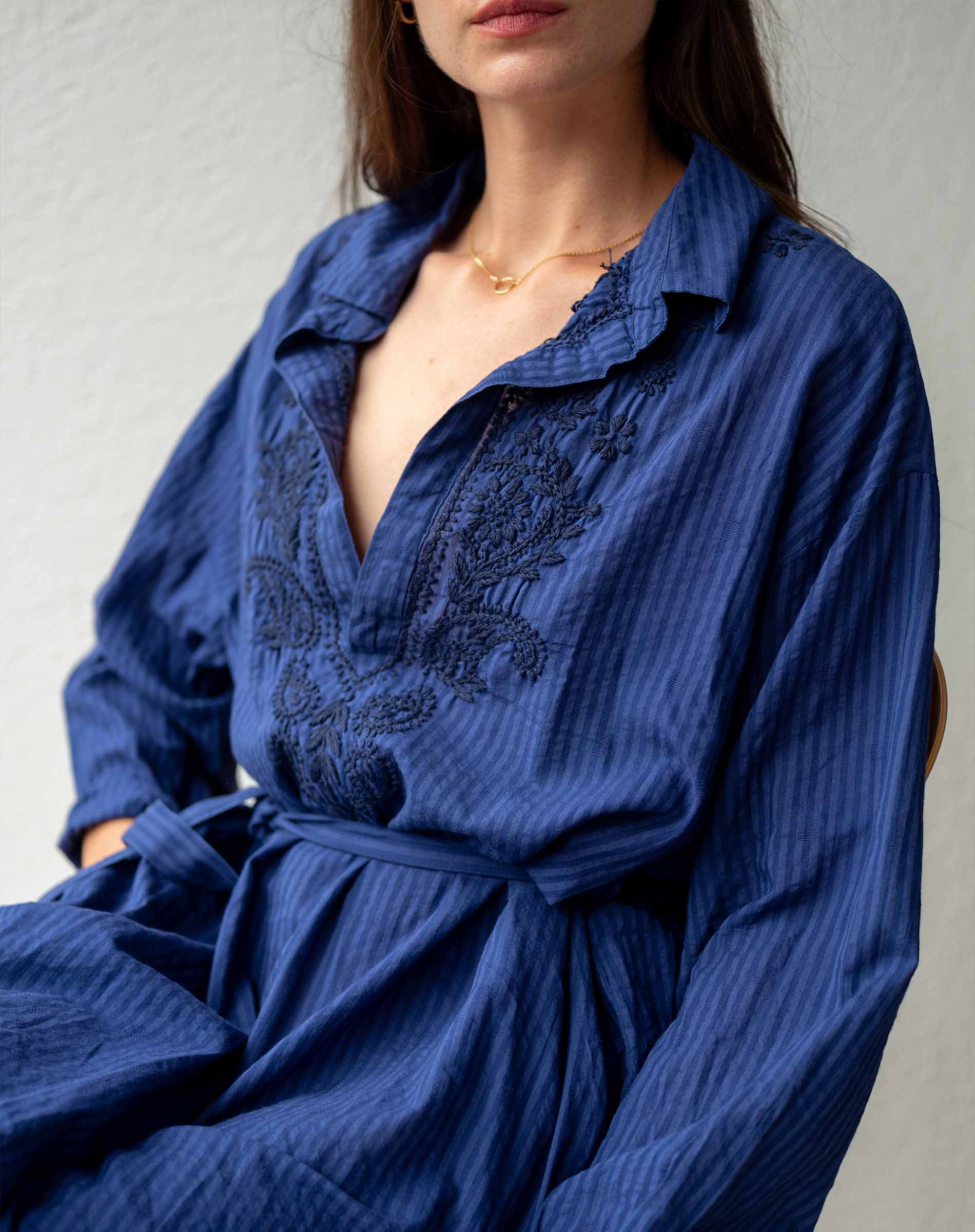 Woman wearing a blue dress with intricate detailing on a plain background