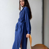 Woman wearing a blue dress holding a wooden chair against a white wall.