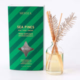Sea Pines reed diffuser in a clear glass bottle with gold-toned sticks and a green striped box featuring the text: 'MERSEA SEA PINES pine | cedar | balsam REED DIFFUSER DIFFUSEUR à BATONNETS MERSEA'. Included additional details at bottom of box are "Inclus de: s tralxated results, 2 Pieces of scented wood, 4 dimensions: 15cm x 10cm x 10cm, Offer included in current promotion" and size '3.4 FL OZ / 100 mL'.