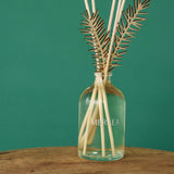 Room diffuser with sea pine leaf accents and a glass bottle featuring the logo.