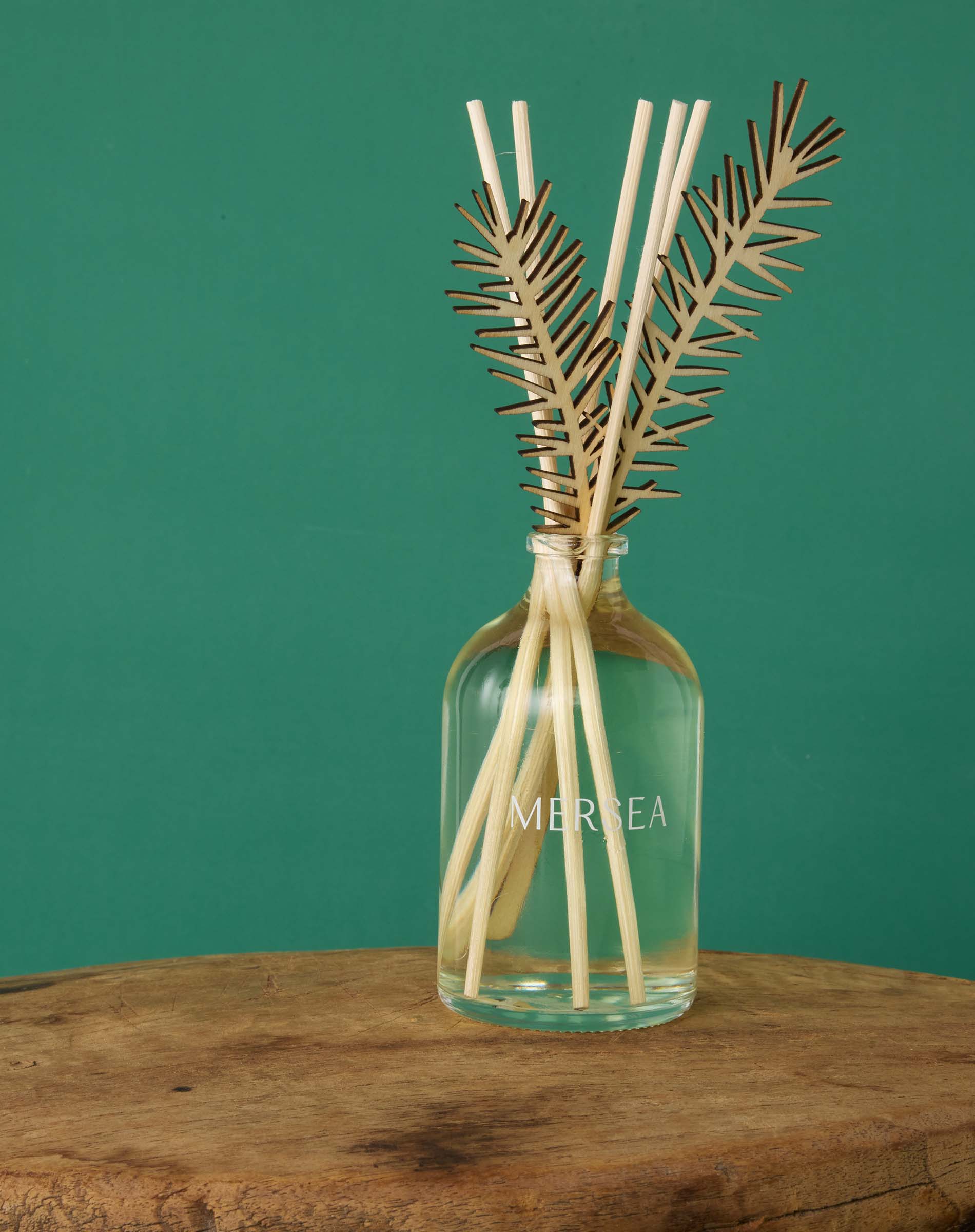 Room diffuser with sea pine leaf accents and a glass bottle featuring the logo.