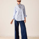 Woman wearing a striped shirt and blue pants against a plain background