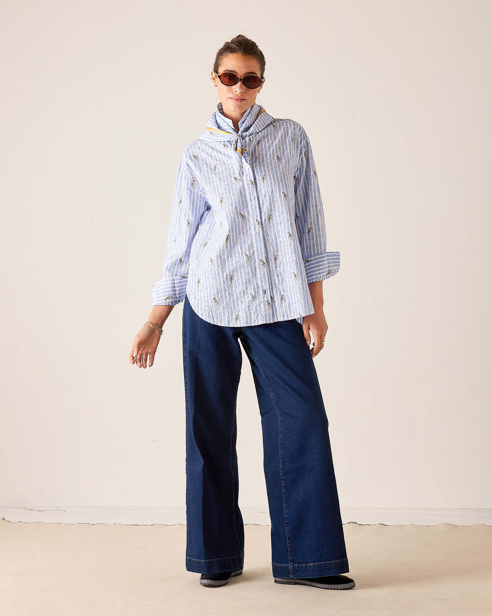 Woman wearing a striped shirt and blue pants against a plain background