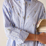 Person wearing a blue and white striped shirt with floral patterns, holding a book.
